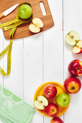 The concept of the diet. The view from the top of the apples lying in the dish, centimeter and a knife on wooden plate