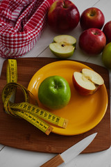 The concept of the diet. Green and red Apple lying in the dish, centimeter and knife on wooden plate closeup