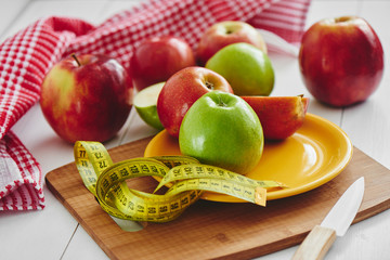 Green and red Apple lying in the dish, centimeter and knife on wooden plate closeup