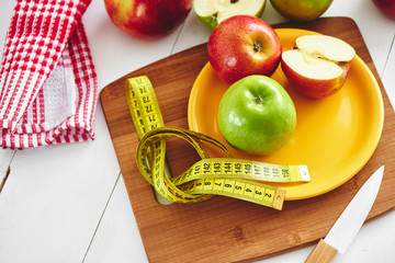 The concept of the diet. Green and red Apple lying in the dish, centimeter and knife on wooden plate closeup