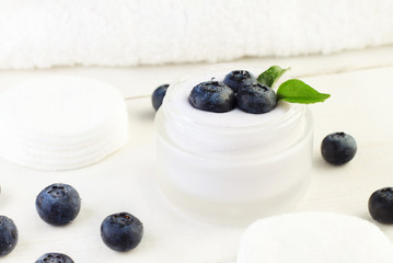 Skincare cream container with fresh indigo blueberries. White and blue tones. Holistic botanical beauty treatment product.