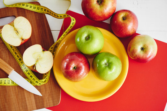The concept of the diet. The view from the top of the apples lying in the dish, centimeter and a knife on wooden plate