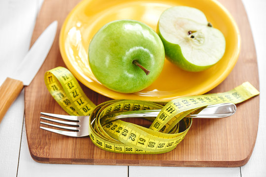 The concept of the diet. Green Apple lies on a plate, knife and fork wrapped in a centimeter on a wooden Board closeup