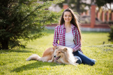 young beautiful woman with long hair sits on the lawn with collie dog. Outdoors in the park.