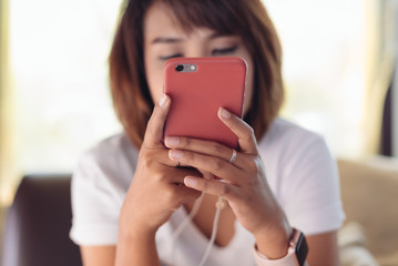 Asian woman looking at smart phone, reading message, sitting on sofa in living room