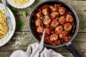 Meatballs in tomato sauce in a frying pan and spaghetti on a wooden rustic table. Delicious lunch, top view