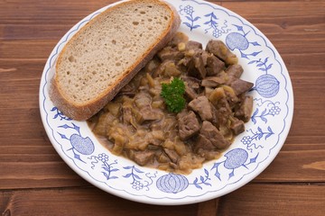 Roasted chopped lamb livers with onion and vine sauce served on old rustic plate and wooden table with slice of artisan bread. Simple dish typical for traditional homemade Czech or Austrian cuisine. 