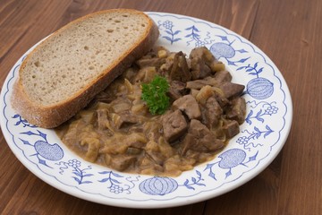 Roasted chopped lamb livers with onion and vine sauce served on old rustic plate and wooden table with slice of artisan bread. Simple dish typical for traditional homemade Czech or Austrian cuisine. 