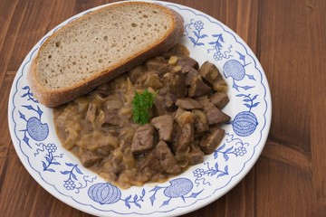 Roasted chopped lamb livers with onion and vine sauce served on old rustic plate and wooden table with slice of artisan bread. Simple dish typical for traditional homemade Czech or Austrian cuisine. 