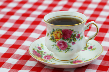 Black tea in colorful vintage cup on checkered cloth with copy space
