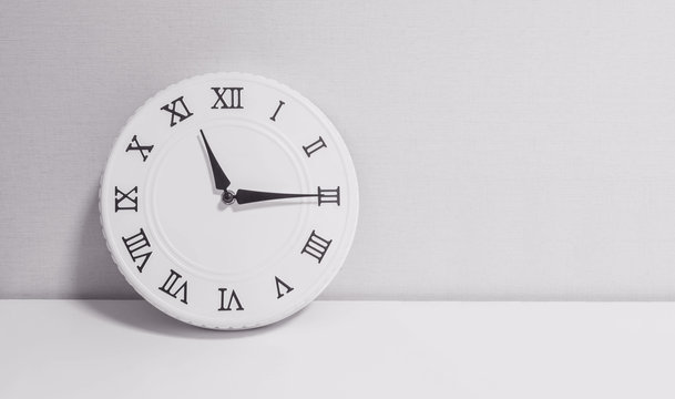 Closeup white clock for decorate show a quarter past eleven o'clock or 11:15 a.m. on white wood desk and wallpaper textured background in black and white tone with copy space