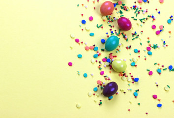 Easter chocolate egg with colorful explosion of candies and sweets on yellow colored background.