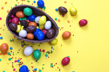 Fototapeta na wymiar Easter chocolate egg with colorful explosion of candies and sweets on yellow colored background.