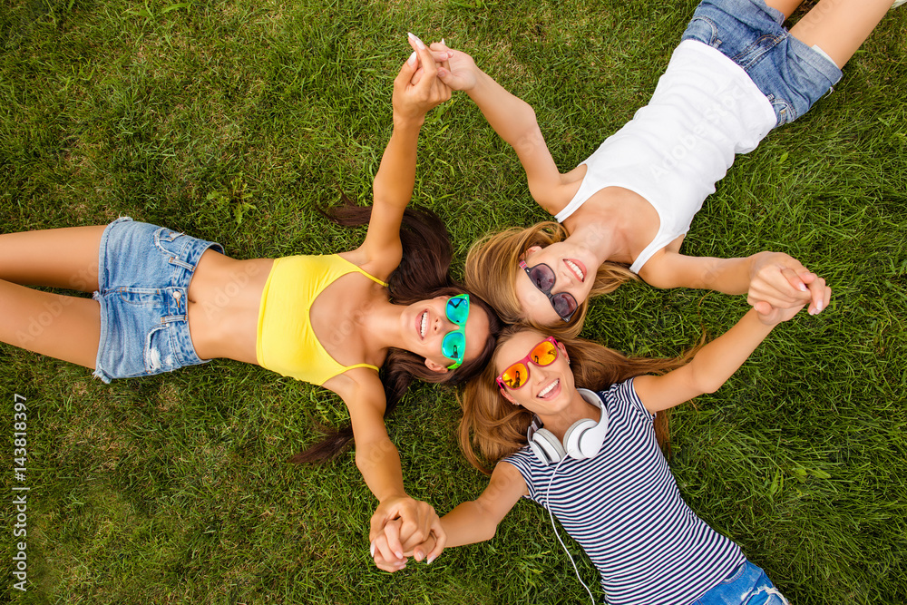 Wall mural Top view of happy girls lying on grass and holding hands