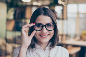 Close up portrait of cheerful smiling smart young pretty woman holding glasses in modern workspace
