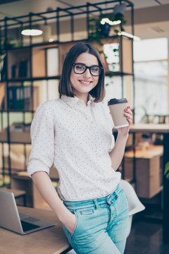 Cheerful smiling smart young pretty woman holding cup of coffee  in modern workspace