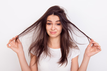 Sad girl showing  her damaged hair while standing white background