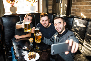 Handsome friends are drinking beer, doing selfie and smiling while resting in pub. Beer time.