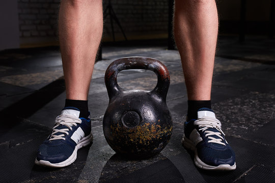 Closeup photo of young man's legs in sneackers and kettlebell against dark background.