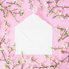 Frame of spring white flowers and white envelope on pink background. Flat lay, top view. Spring time background.