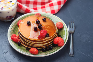 Stack of pancakes with frozen berries and honey on black background. Selective focus.