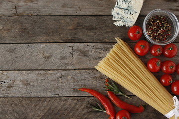 Italian pasta spaghetti and cooking ingredients cherry tomatoes parmesan greens. Italian food background. Top view with copy space