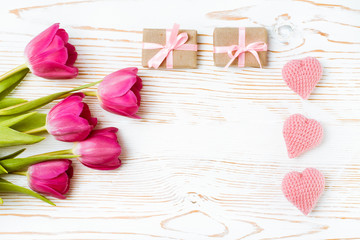 Вязанные сердца, подарки с розовой лентой и букет тюльпанов на белом деревянном фоне