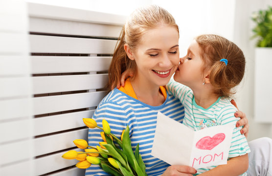 Happy mother's day! Child daughter congratulates moms and gives her a postcard and flowers