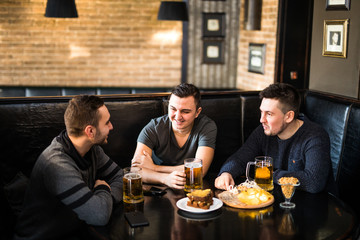 Fototapeta na wymiar Meeting at the pub. Three happy friends drinking beer at the traditional pub