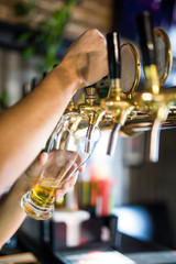 Mans hand pouring pint of beer behind the bar in pub