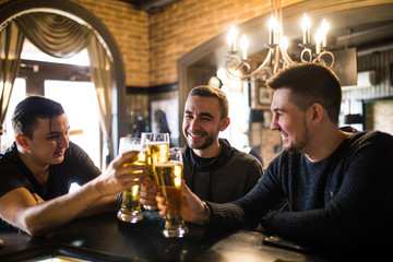 Friends in bar. Three happy young men in casual wear talking and drinking beer while sitting at the bar counter together