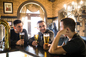 Cheerful old friends having fun and drinking draft beer at bar counter in pub. Friends meet