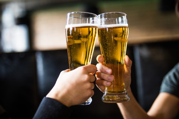 Men cheers with beer in glasses in pub. Close up. - obrazy, fototapety, plakaty