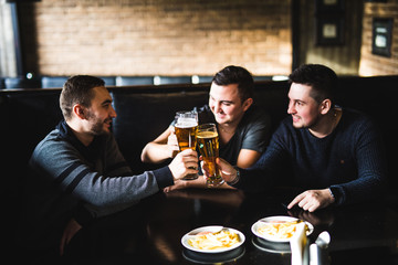 Men friends meet in pub and drink beer and eat chips. Cheers and have fun in england pub.