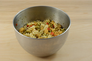 Vegetable rotini pasta salad with herb spice salad dressing in stainless steel mixing bowl