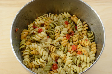 Vegetable rotini pasta salad with herb spice salad dressing in stainless steel mixing bowl