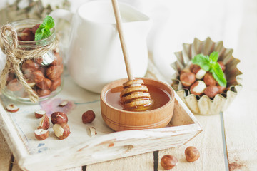 Honey in the wooden bowl, mint leaves, hazelnuts and jar with milk on the wooden tray
