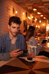 Handsome millennial with cellphone in restaurant
