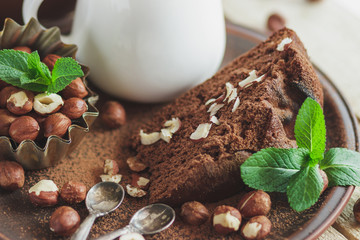 Piece of chocolate cake, mint leaves, hazelnuts and jar with milk