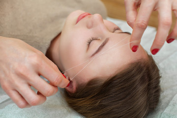 Master corrects makeup gives shape and thread plucks eyebrows in a beauty salon. Professional care for face.