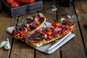 Toasts with jerky meat on a piece of paper. Rustic surface of wooden tabletop in the background.