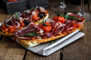 Toasts with jerky meat on a piece of paper. Rustic surface of wooden tabletop in the background.