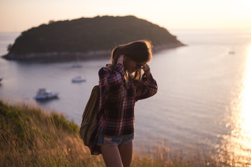Hipster stylish woman traveler looking on a sea or ocean at the sunset