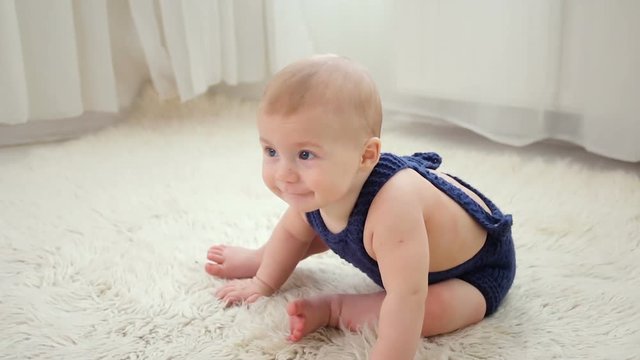 little baby boy of five months, crawling on the floor in the blue knit jumpsuit