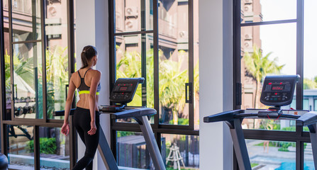 Horizontal shot of woman jogging on treadmill at health sport club at luxury resort. Female working out at a gym running on a treadmill with a great summer view at spa facility at hotel during summer