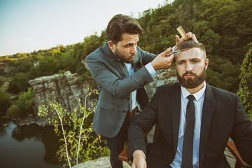 Handsome barber giving his customer a haircut on the edge of a canyon