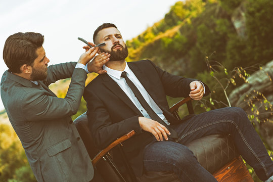 Professional barber shaving his client on the edge of a mountain