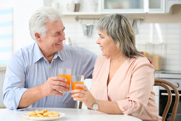 Fototapeta na wymiar Beautiful mature couple with orange juice sitting at kitchen table