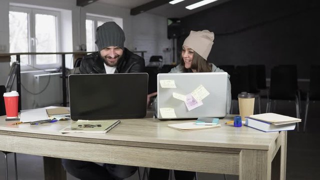 Young man and woman working in creative office. White and black laptops on the table. Modern design of the office. Shot in 4k