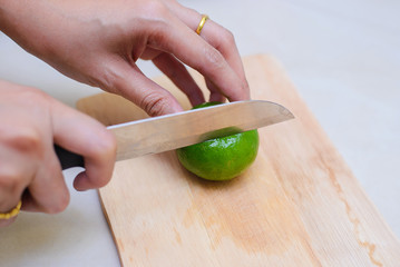 Hands slicing a lime with a chef knife on a cutting board